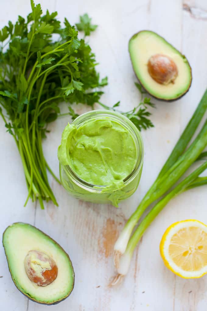 green goddess dressing in mason jar on white board with avocado, lemon, scallion, parsley