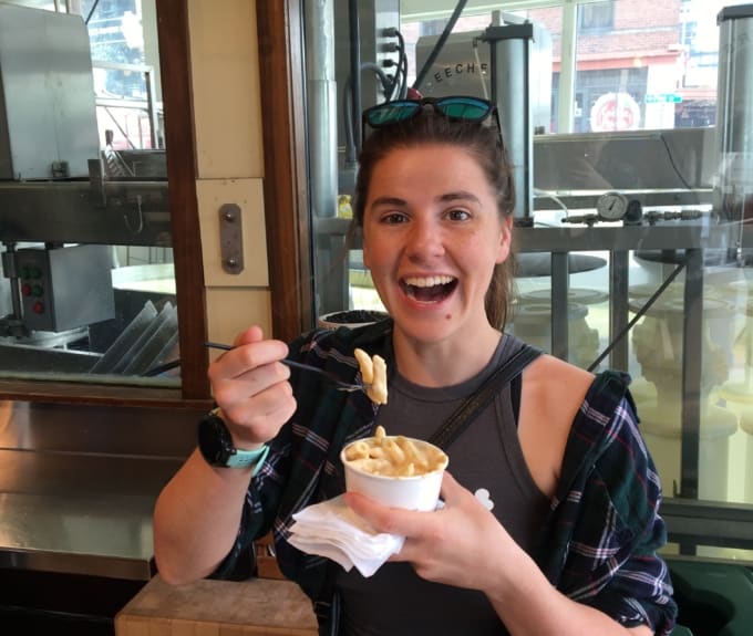 woman with sunglasses on head eating macaroni and cheese out of a small cup