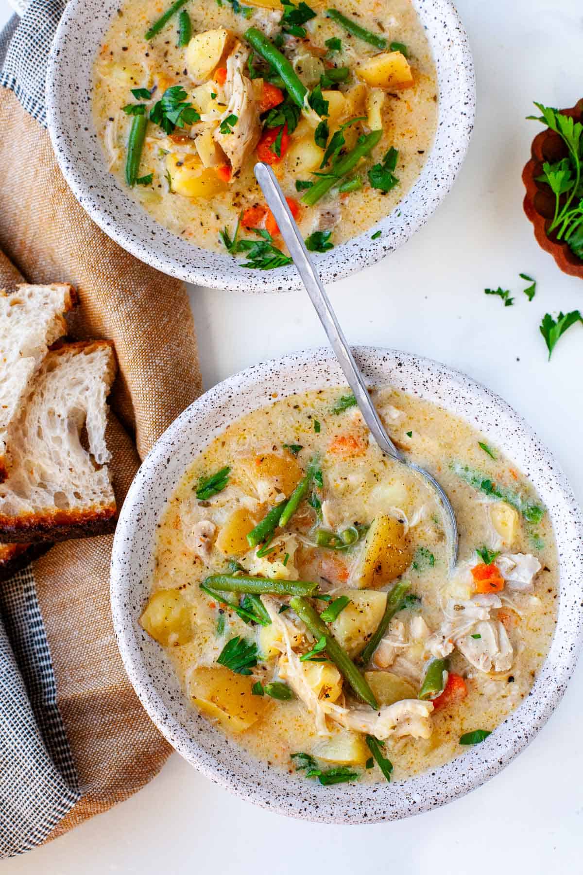 two bowls of Instant Pot Chicken Stew on a white surface beside a kitchen towel with two slices of bread